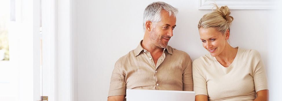 A photo of a mature couple looking at a laptop and smiling — Central Quest, the matchmaking agency for accomplished divorced men